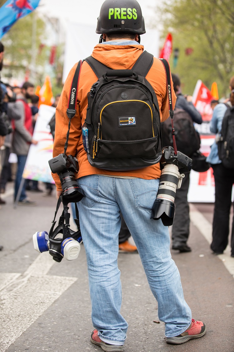 Image of a reporter in a helmet in front of protesters in the middle of a street.
