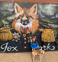 Dr. Magic Wade pictured with her dog in front of a painted mural of a fox on a brick wall