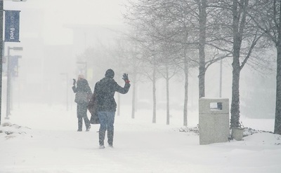 Two students waving goodbye on the quad during a snow storm
