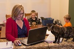 Woman working on laptop at home with family in the background